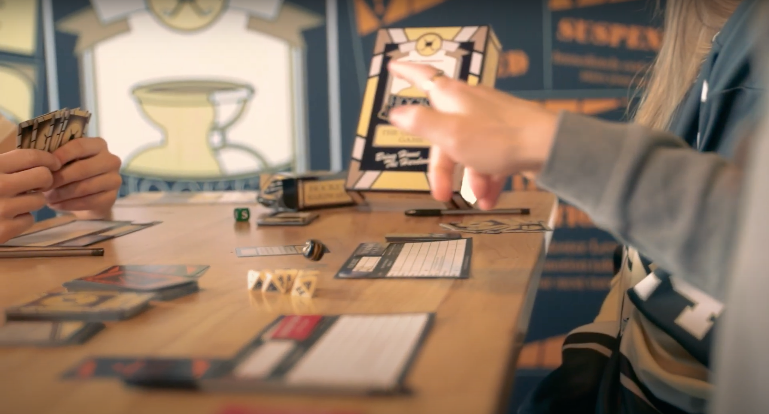 Three people playing Hockey Hardware with cards and pieces on a table. One of these players is rolling the black Game Die.